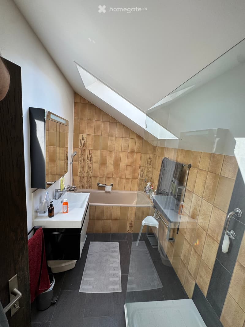 Modern bathroom with a bathtub, sink, mirror, and glass shower enclosure. Features include a towel, stool, and bathroom cabinet.