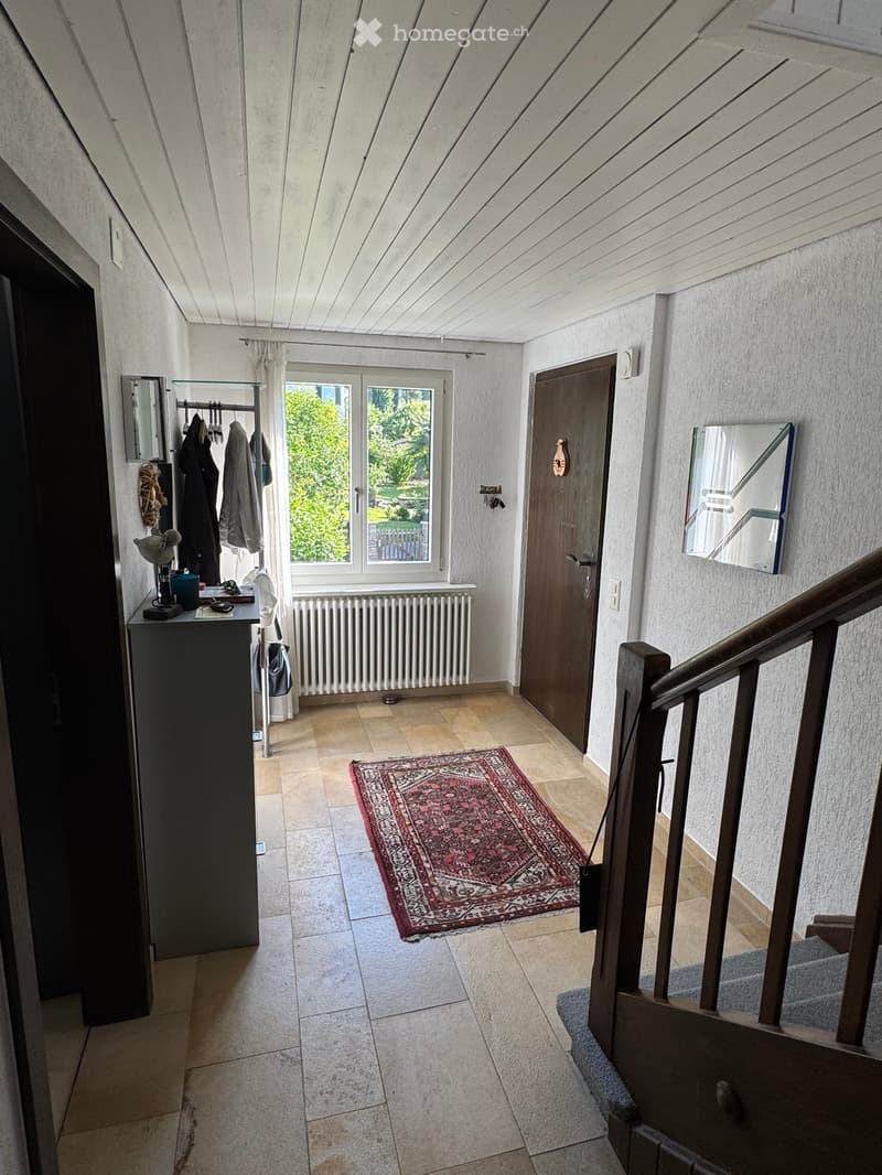Hallway with tiled floor, staircase, window, coat rack, and small table with items on it.