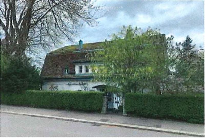 Detached house, brick, multiple windows, roof covered with green, entrance gate, bushes in the front
