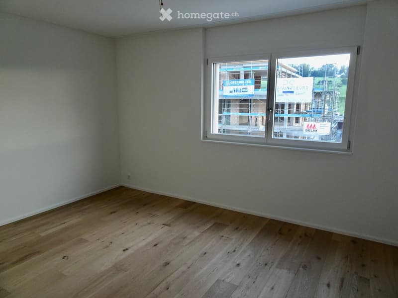 Empty room with wooden flooring and large window showing construction site outside.