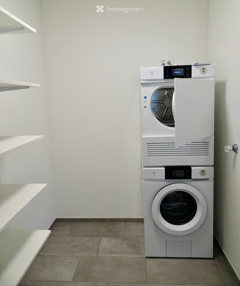 Modern bathroom with a stacked washer and dryer unit, white walls, and tiled floor.