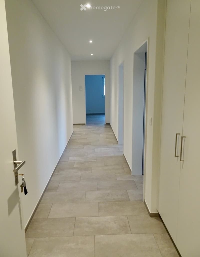 Empty hallway with tiled floor, white walls, and several doors, including one with a visible key and lock.