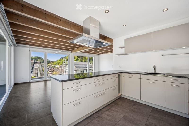 Modern kitchen with white cabinets, stainless steel range hood, and a black countertop, featuring large windows with a scenic view.