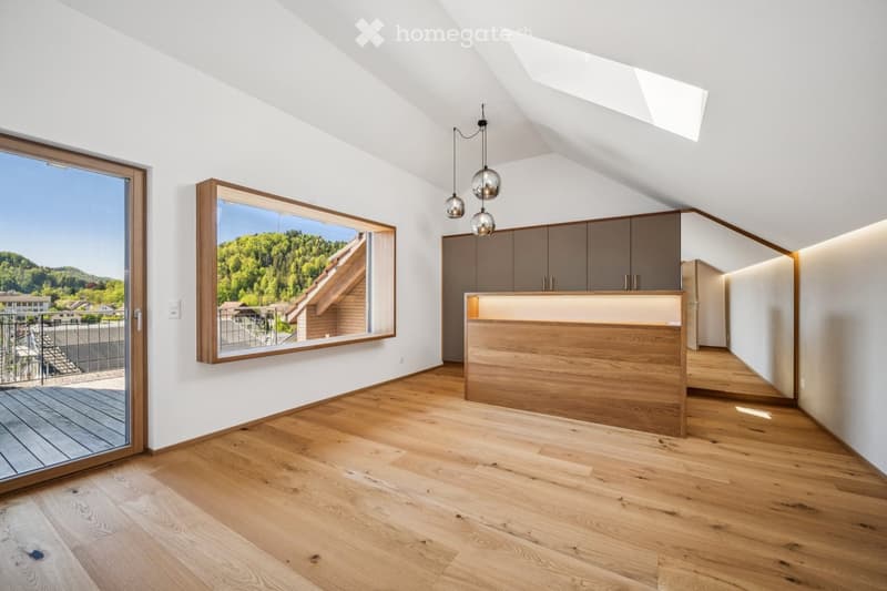 Bright, airy room with wooden flooring, large windows, and modern cabinetry. Features pendant lights and a view of a green landscape.