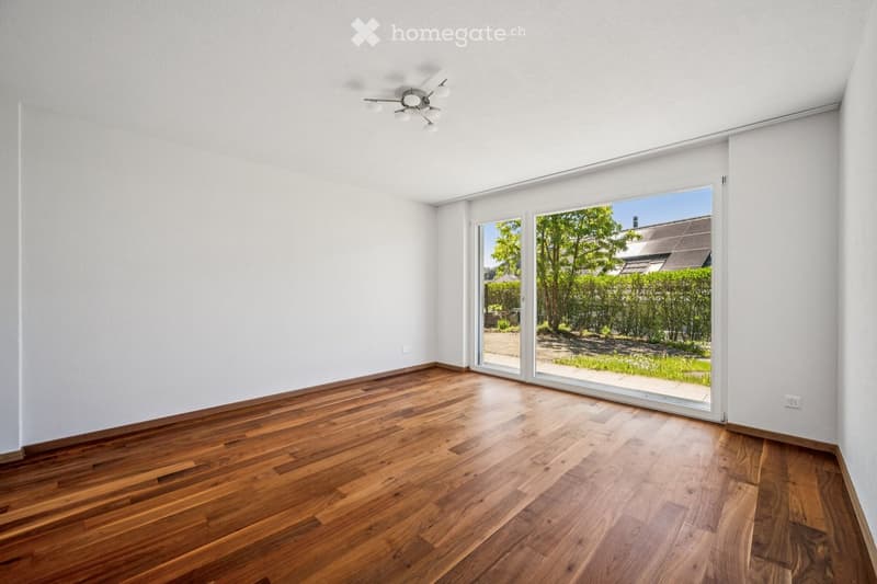 Empty room with wooden flooring, white walls, and large sliding glass doors leading to a garden area.