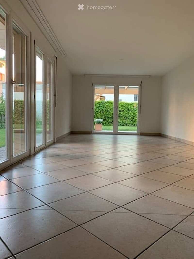 Empty room with large glass doors leading to a garden, tiled floor, and neutral-colored walls.
