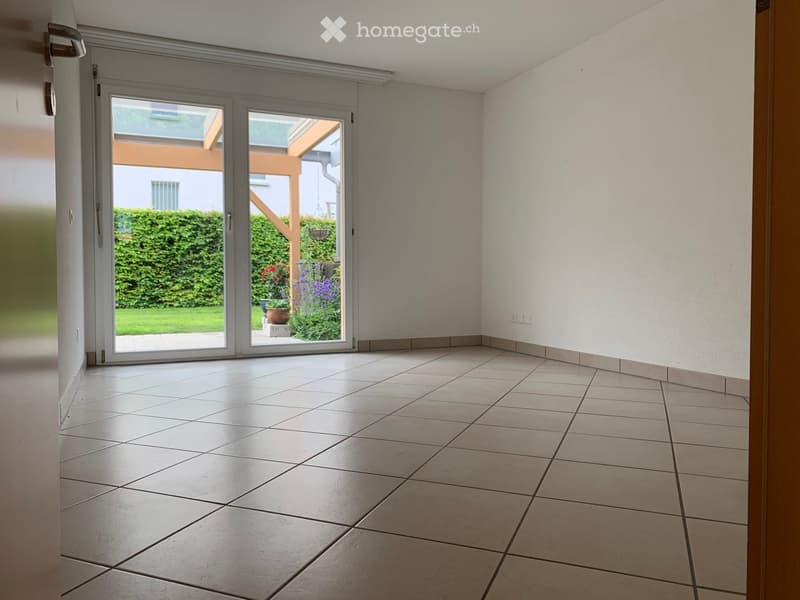 Empty room with tiled floor, white walls, and large sliding glass doors leading to a garden area.