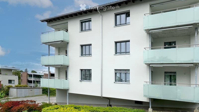 Modern multi-story apartment building with white facade, multiple windows, and glass-enclosed balconies.