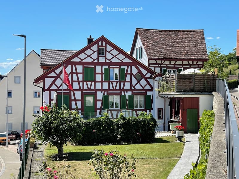 Traditional two-story house with red and white timber framing, green shutters, and a well-maintained garden.