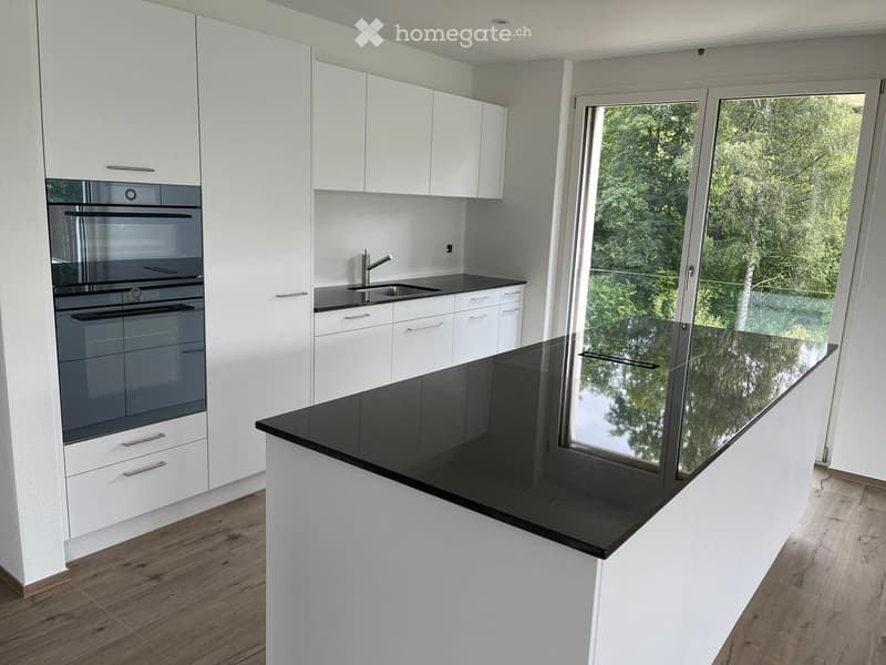 Modern kitchen with white cabinets, black countertops, and a large window overlooking greenery.