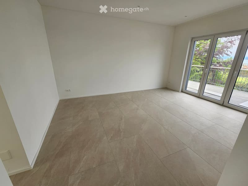 Empty room with light-colored tiled flooring and white walls, featuring a large sliding glass door leading to a balcony.