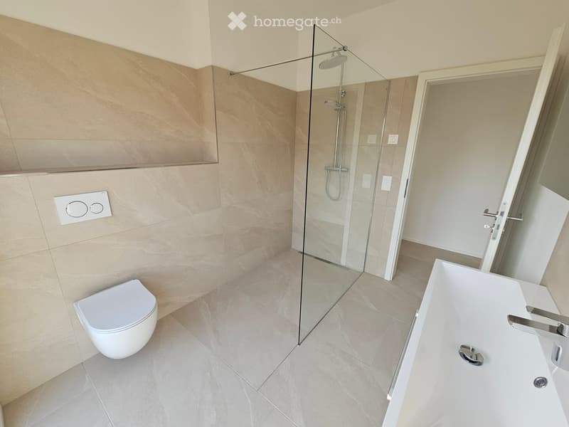 Modern bathroom with beige marble tiles, a white toilet, a bathtub, and a glass-enclosed shower area.