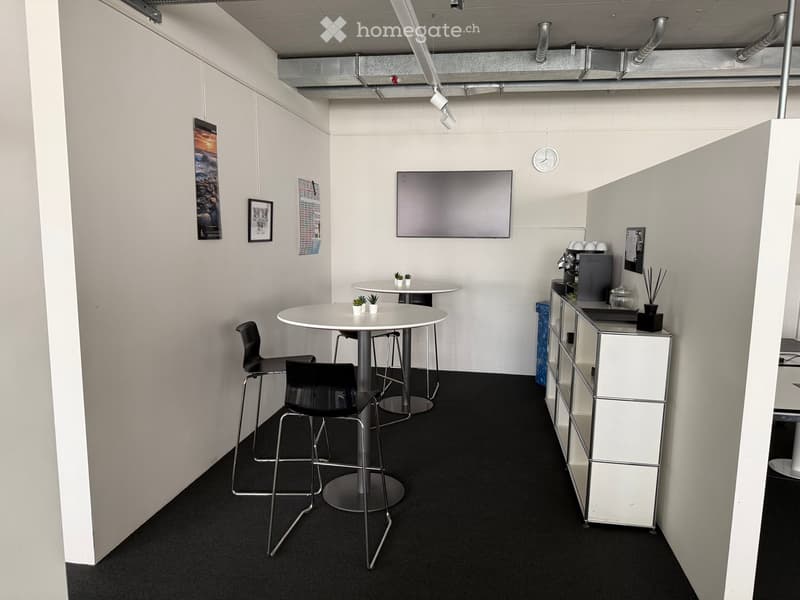 Modern break room with white walls, black carpet, round tables, chairs, a TV screen, a cabinet, and small potted plants.