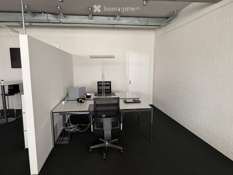 Modern office space with white brick walls, black carpet, desks, chairs, and a standing lamp.