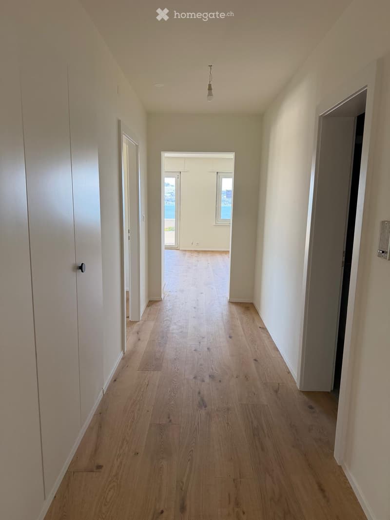 Empty hallway with light wooden flooring, white walls, and several doors leading to other rooms.
