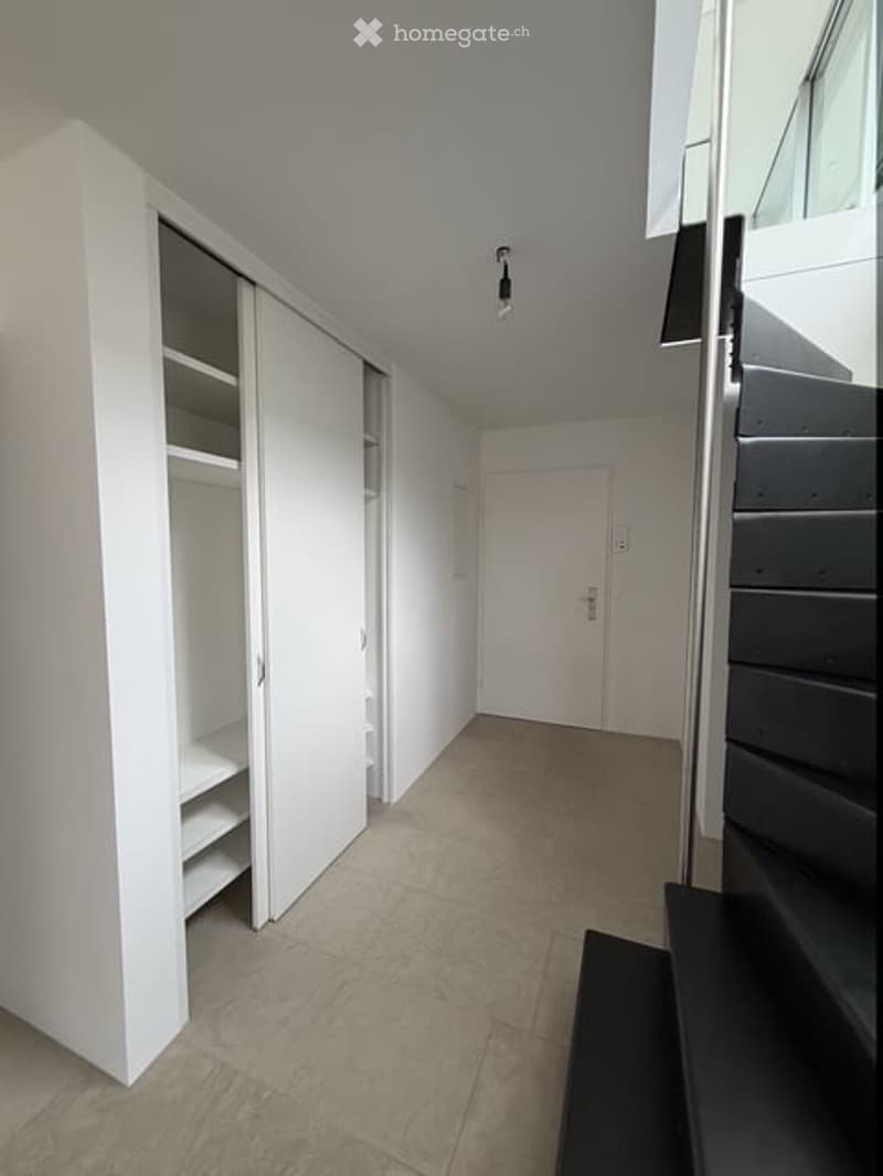Modern hallway with white walls, light-colored tiled floor, built-in white closet with open shelving, and a staircase leading upwards.