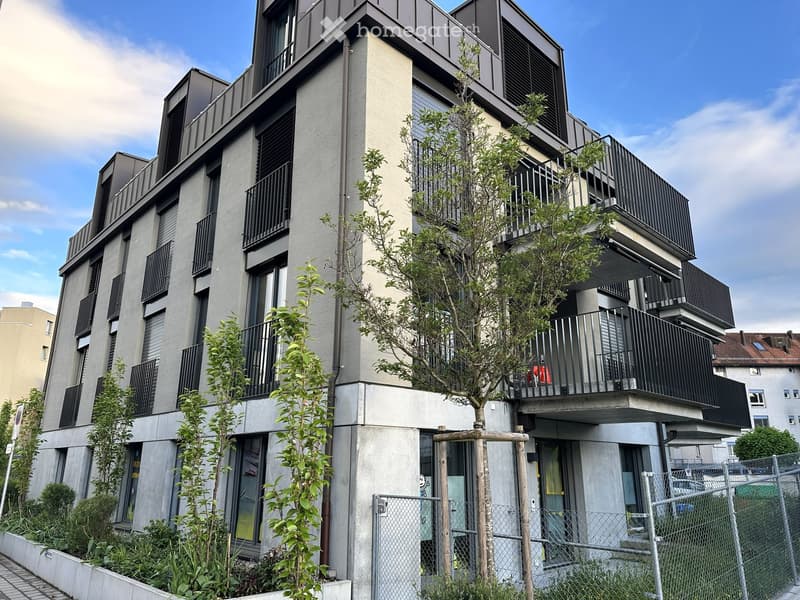 Building. Modern multi-story building with balconies, large windows, and contemporary design, surrounded by greenery and a fence.