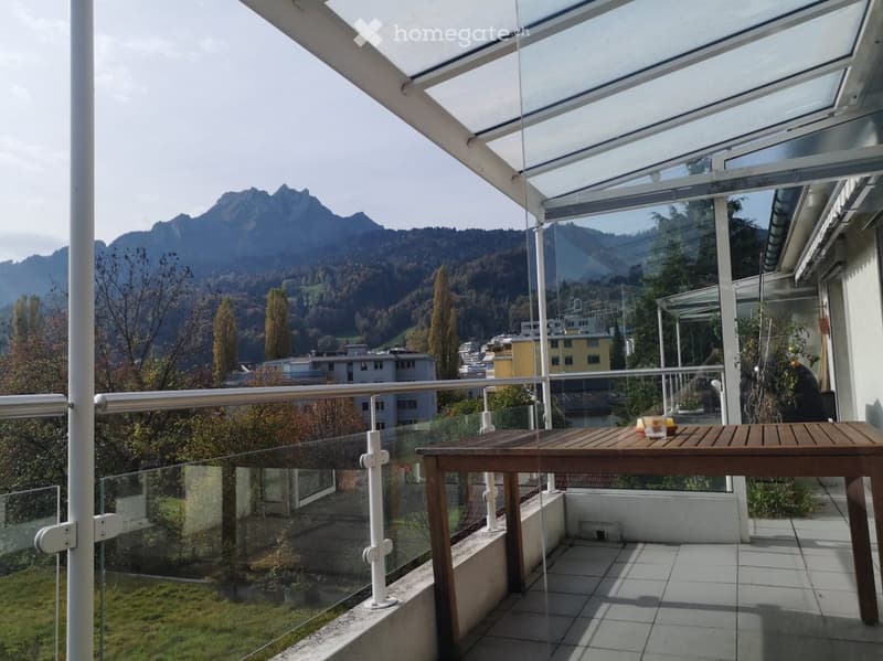 Balcony with a wooden table, glass railing, and scenic mountain view.
