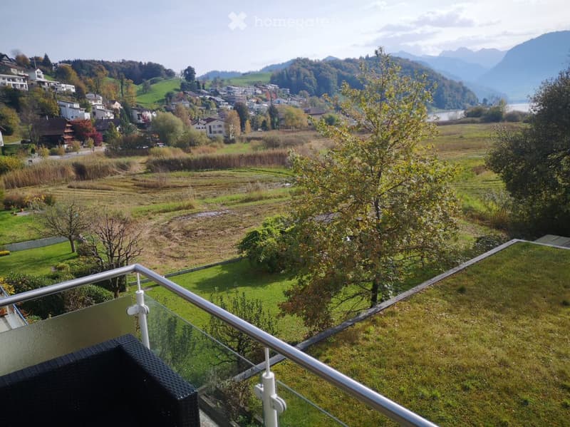 Balcony with glass railing overlooking a scenic valley, town, and mountains.