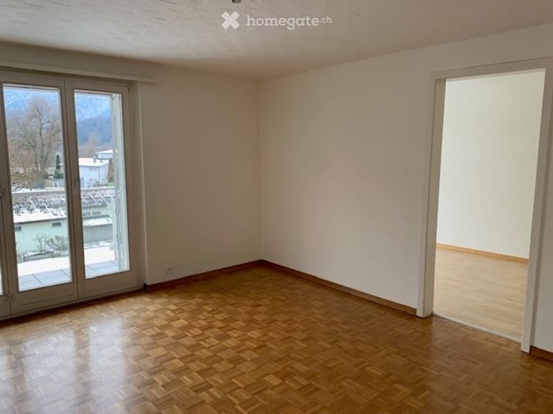Empty room with wooden flooring, large windows offering a scenic view, and white walls.