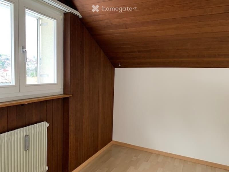 Empty room with wooden walls, wooden floor, white walls, and a window with a view.