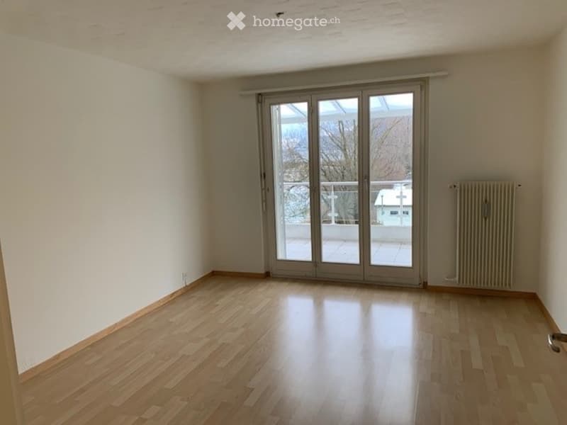 Empty room with wooden flooring, large sliding glass door leading to a balcony, and white walls.