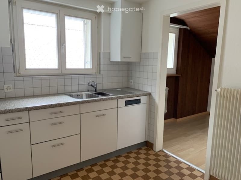 Bright kitchen with white tiled walls, granite countertop, stainless steel sink, and built-in dishwasher. The floor features a classic checkered pattern.