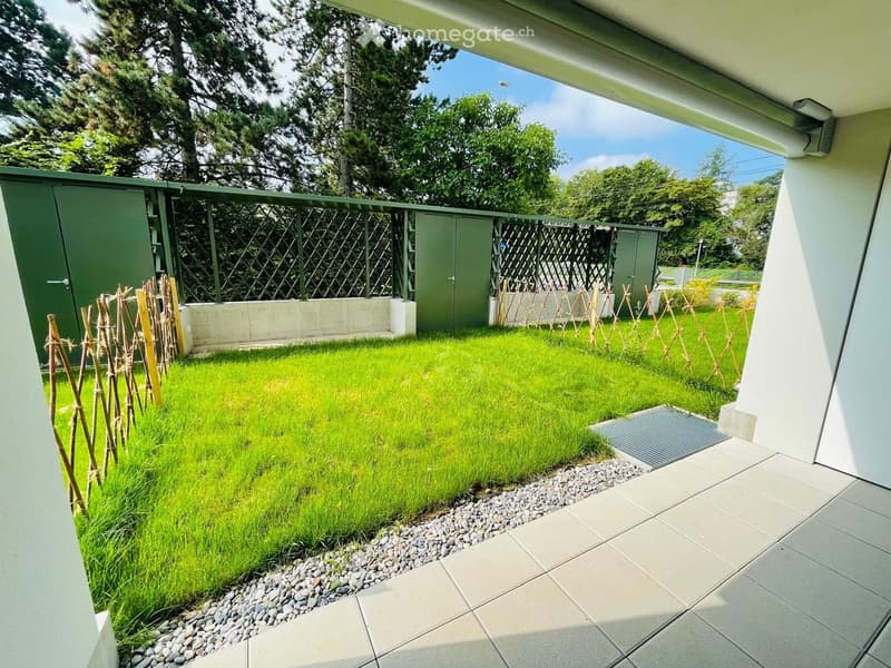 Well-maintained garden with a neatly trimmed lawn, gravel border, and wooden trellis structures. Green fence and modern building elements visible.