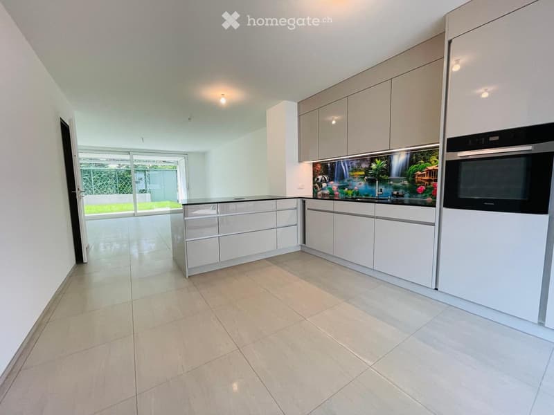 Modern kitchen with white cabinets, a built-in oven, and a sink, featuring a scenic waterfall backsplash design and large windows overlooking a garden.