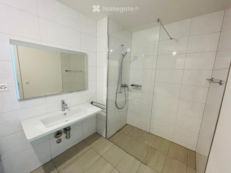 Modern bathroom with white tiles, a glass-enclosed shower, a single sink with a modern faucet, and a large mirror with built-in storage.