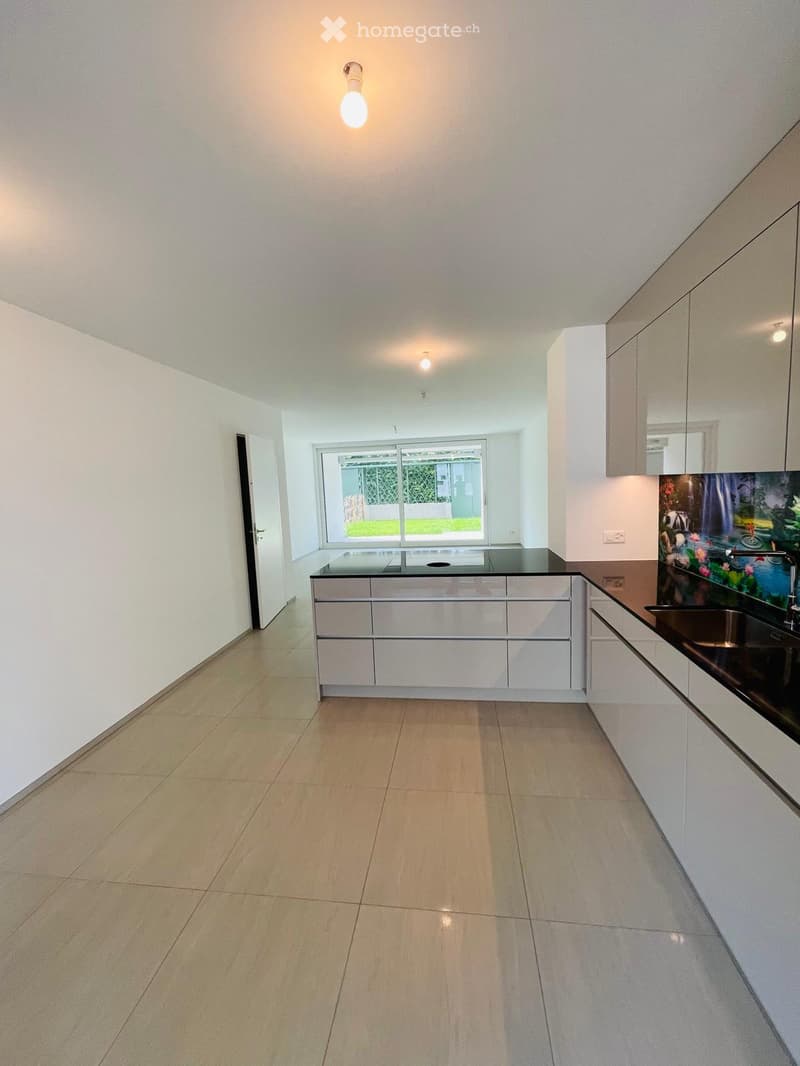 Modern kitchen with white cabinets, a black countertop, and a large window overlooking a garden. The floor is tiled, and the space is well-lit with ceiling lights.