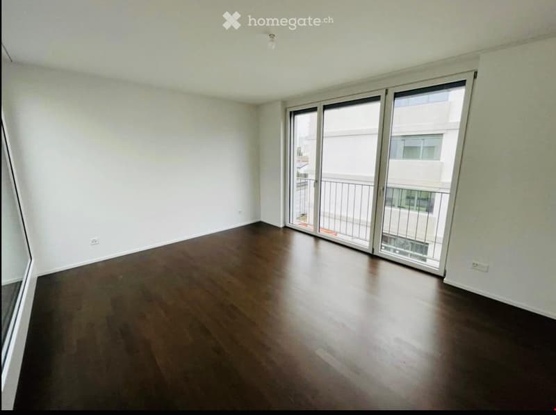 Empty room with wooden flooring and large sliding glass doors leading to a balcony.