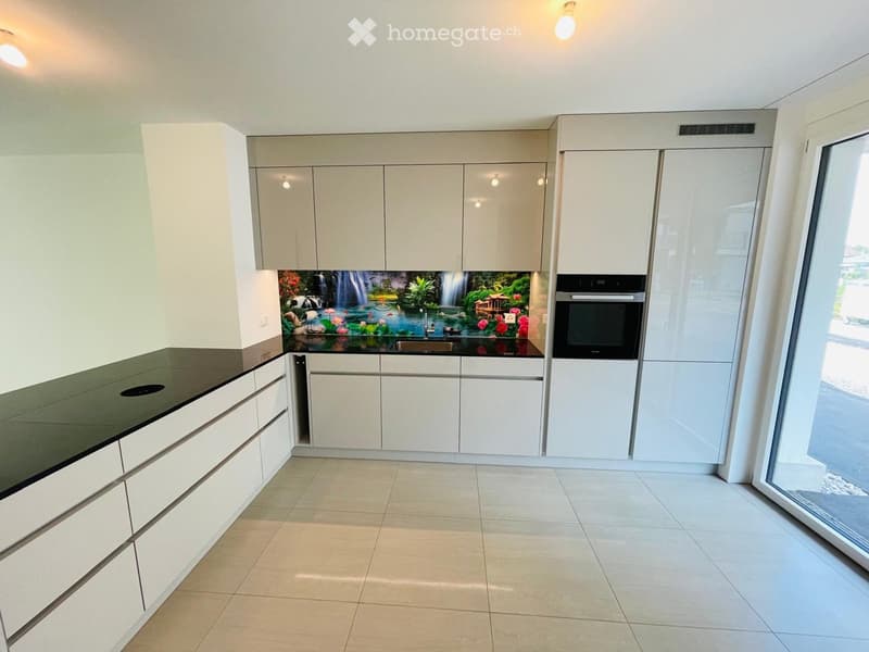 Modern kitchen with white cabinets, dark countertop, and a decorative backsplash featuring a waterfall design. Includes a sink and an oven.