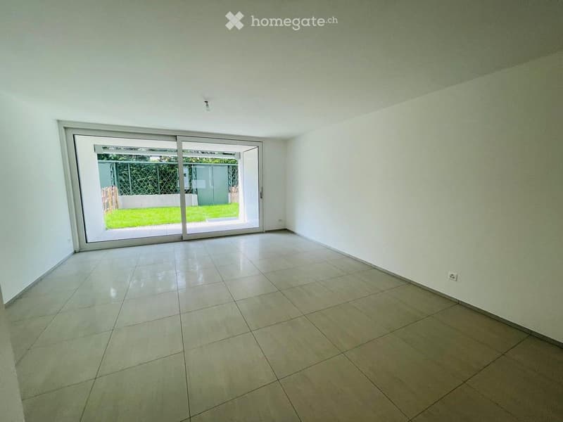 Empty room with tiled floor, white walls, and large sliding glass doors leading to a garden area.