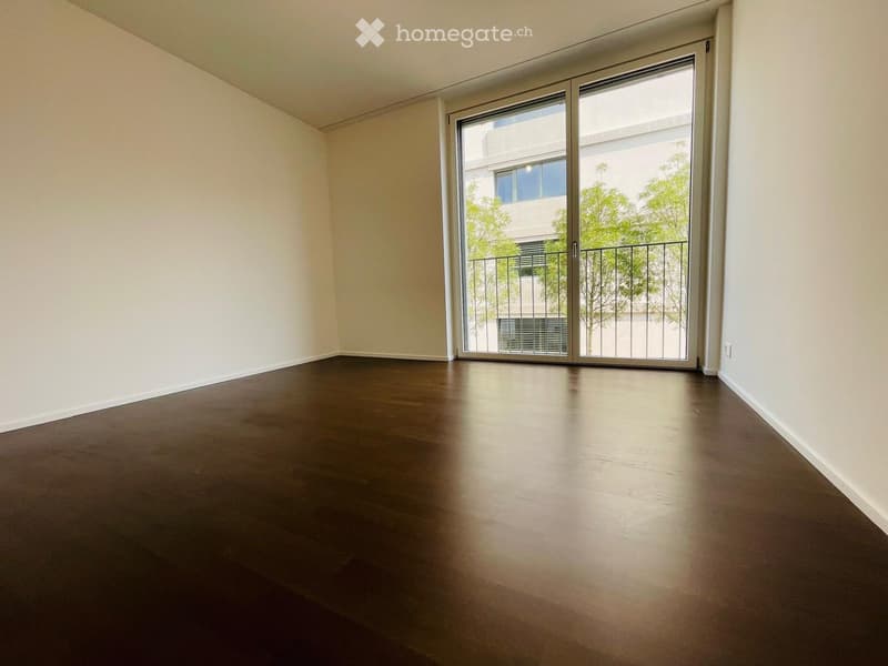 Empty room with dark wooden flooring, white walls, and large sliding glass doors leading to a balcony.