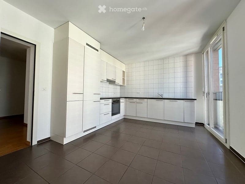 Modern kitchen with white cabinets, dark tiled floor, and built-in oven. Features a large window and sleek design.