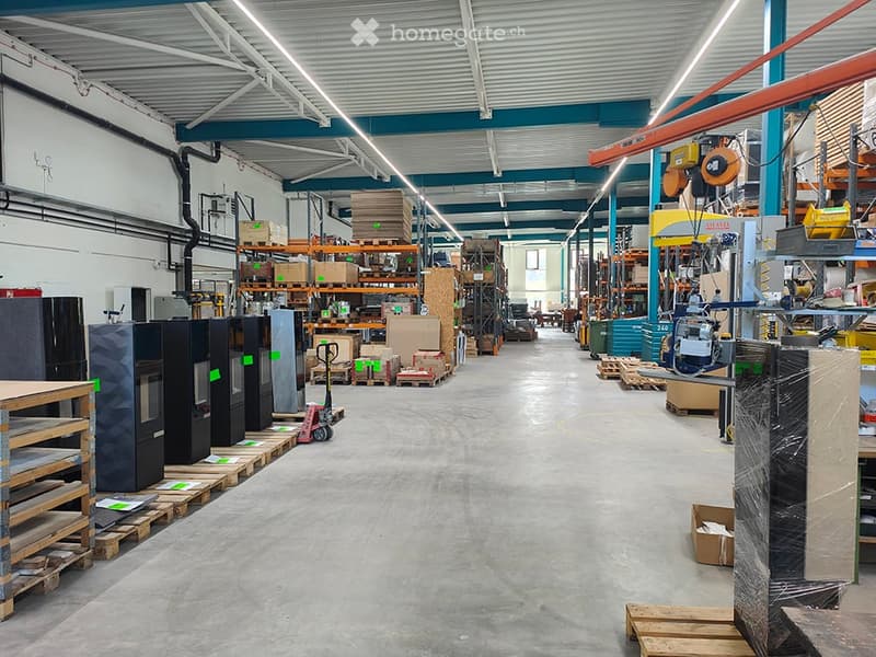 A spacious industrial warehouse with high ceilings, metal shelving units, and various machinery and equipment. Pallets and cabinets are arranged throughout the space.