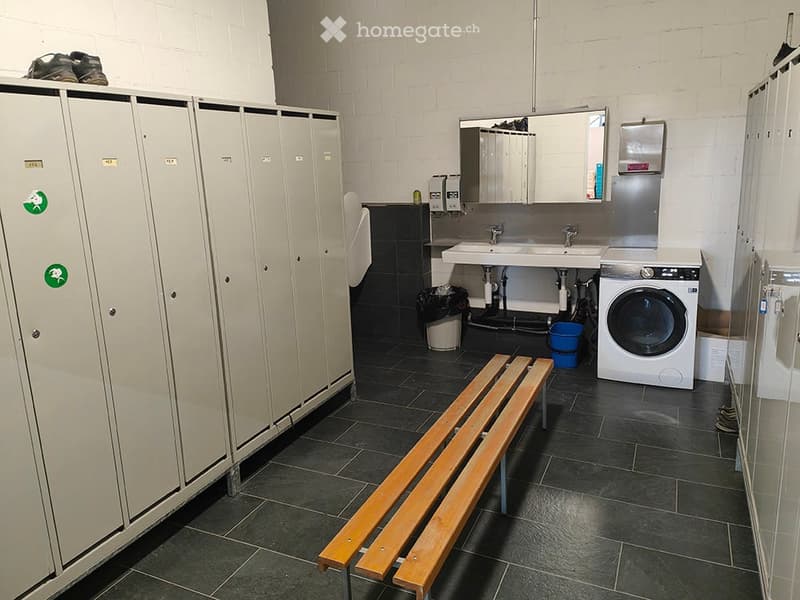 Bathroom with two sinks, a mirror, a wooden bench, lockers, and a washing machine.