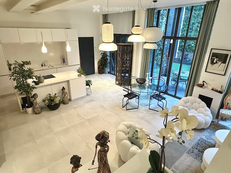 Modern living room with white sofa, glass dining table, pendant lights, kitchen island, and decorative items including statues and vases.