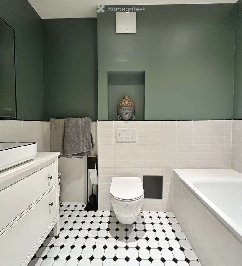 Modern bathroom with white tiles, hexagonal black and white floor tiles, a toilet, bathtub, sink, and a decorative statue on the wall.