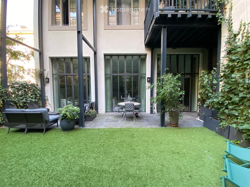 Courtyard with artificial grass, outdoor seating area including a sofa, table, and chairs, surrounded by potted plants and modern building architecture.