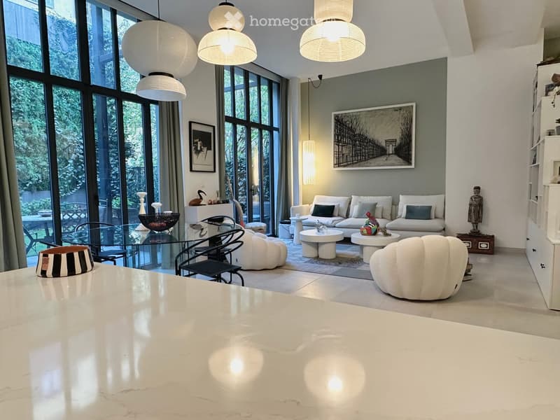 Modern living room with large windows, white sofa, glass coffee table, decorative items, and modern lighting.