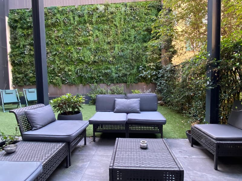 A well-maintained garden with a seating area featuring a sofa, chairs, and a table, surrounded by lush greenery and potted plants.