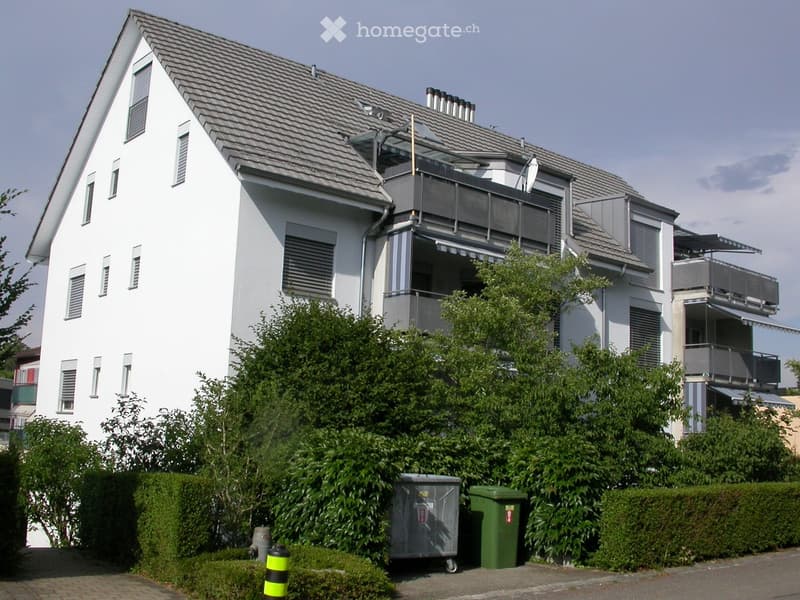 Modern two-story house with white exterior, multiple windows, balconies, and surrounding greenery.