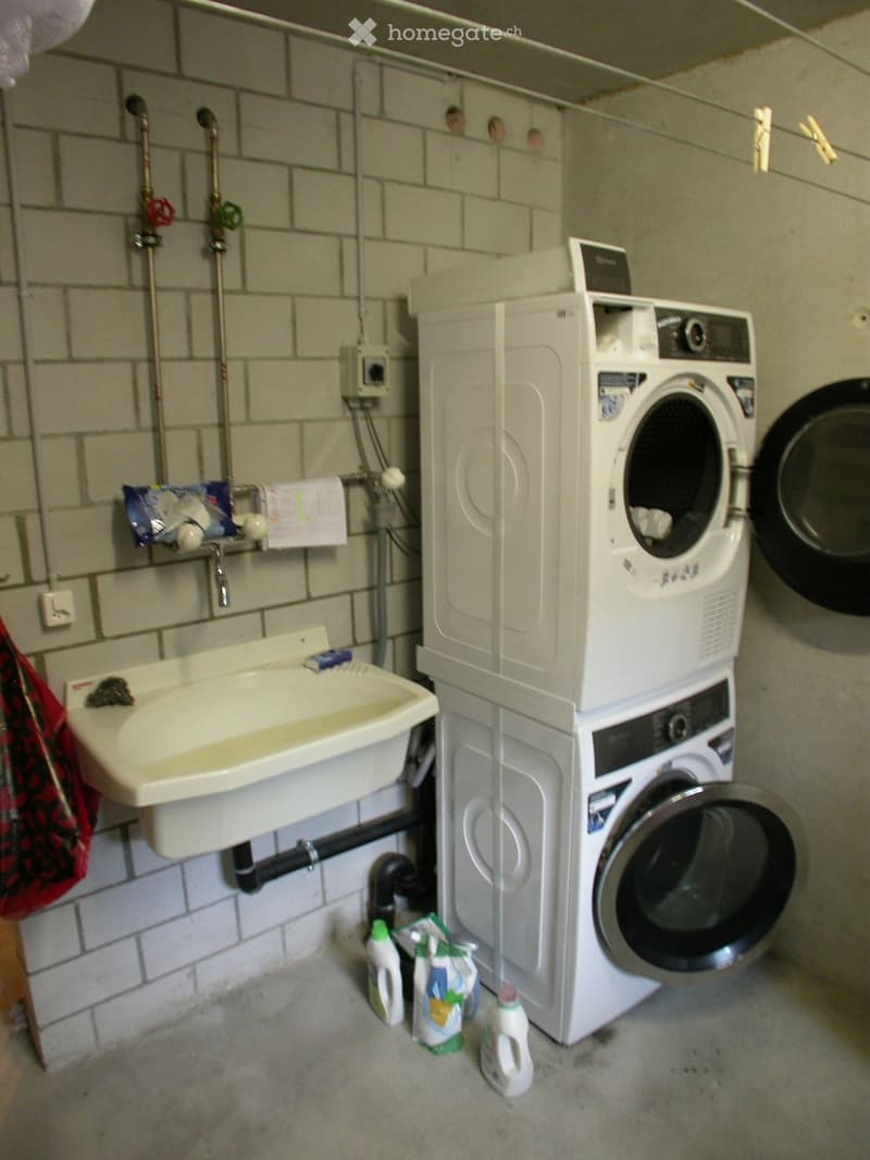 Utility room with a sink, washing machine, dryer, and cleaning supplies on the floor.