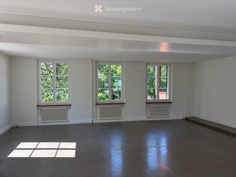 Empty room with wooden flooring, white walls, and three windows with radiators beneath them. No furniture or equipment present.