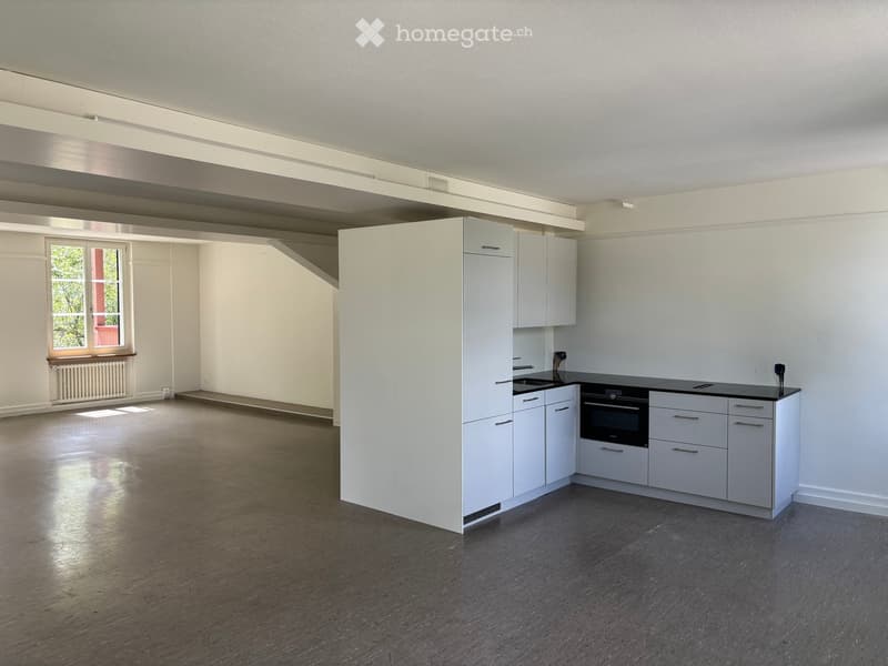 Modern kitchen with white cabinets, black countertop, and built-in oven. The space features wooden flooring and large windows allowing natural light.