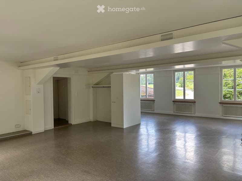 Empty room with polished wooden floor, white walls, large windows, and a door leading to another space.