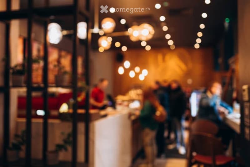 Blurred image of a modern restaurant or cafe interior with warm lighting, a counter, and patrons seated at tables.