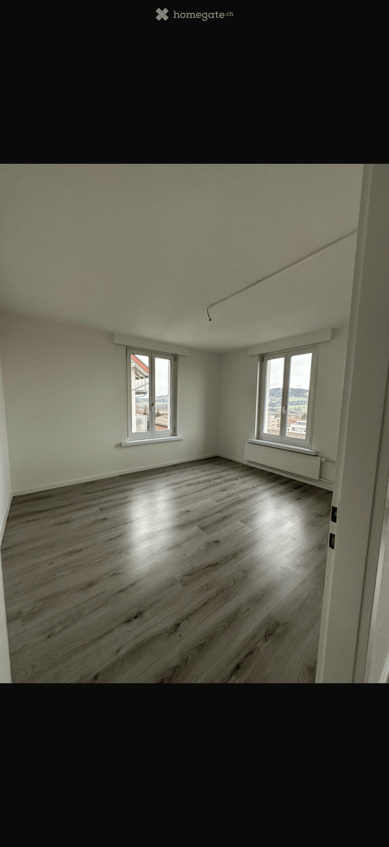 Empty room with light green walls, wooden flooring, and two windows with white frames. No furniture or equipment is present.